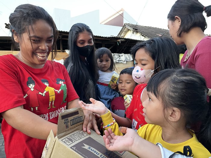 Children crowd around Ince as she opens a box.